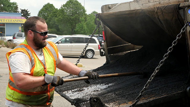 A Public Works employee shoveling pothole asphalt fill.