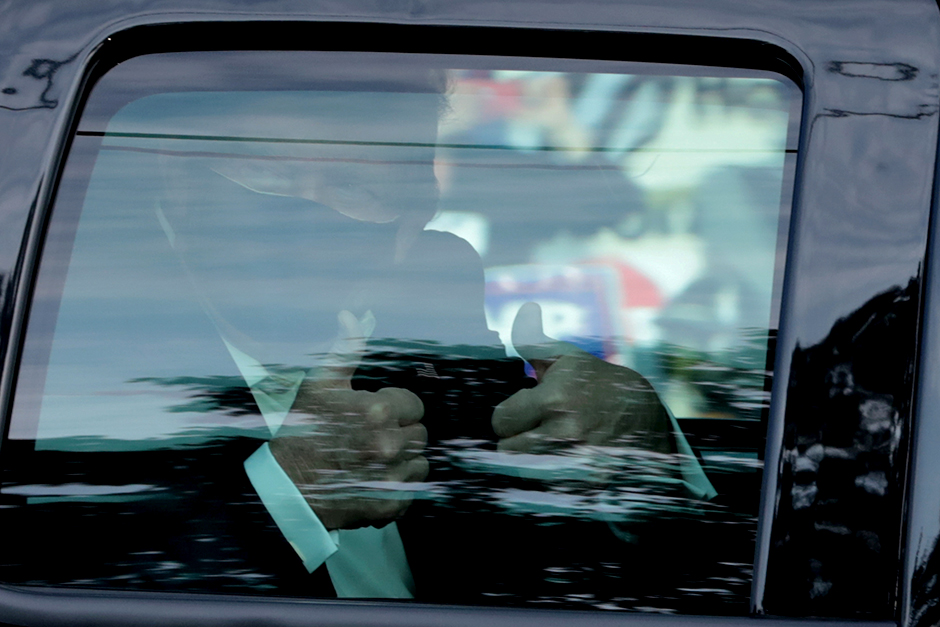 President Donald Trump gestures from a car as he rides in front of the Walter Reed National Military Medical Center on Sunday.