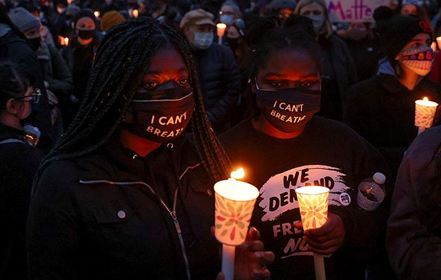 Protesters wearing face masks reading "I can't breathe" hold candles outside the Brooklyn Center Police Department.