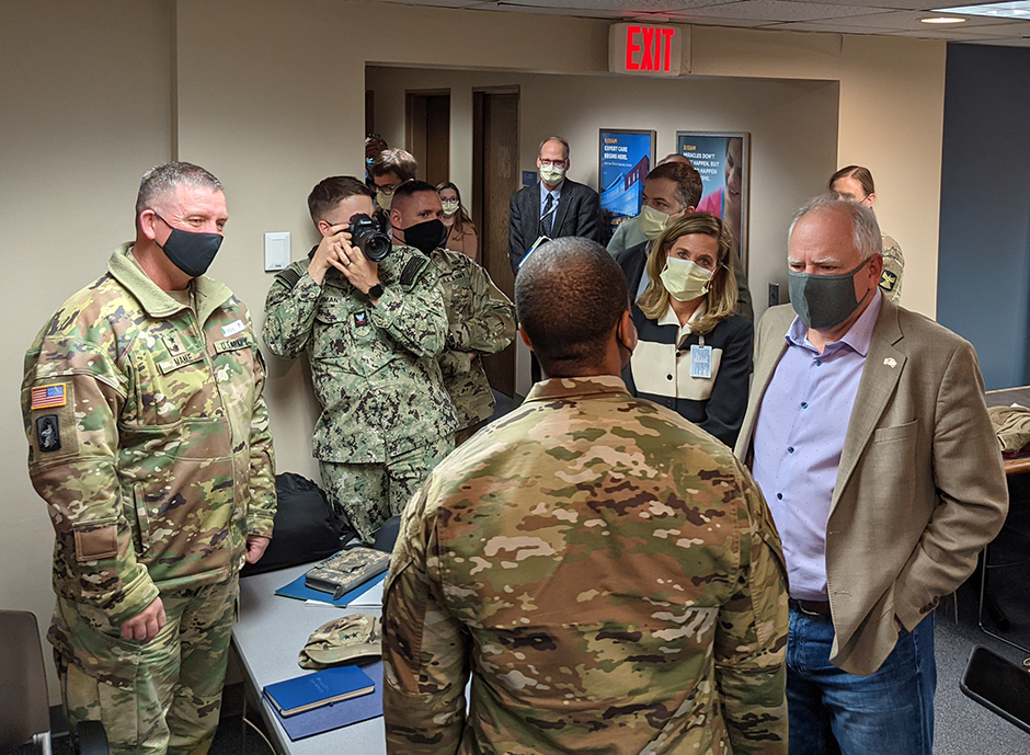Gov. Tim Walz, right, speaking to medical team members from the Department of Defense, as Major General Shawn Manke, far left, looks on.