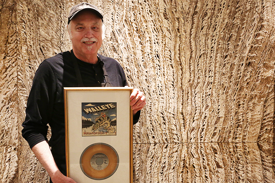 Rich Lewis, a former member of the Hula-Poppers, holding a framed copy of the “Walleye” single, which he said a friend spraypainted gold.