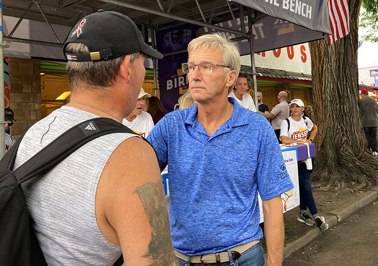 Scott Jensen’s meeting and greeting of voters, however, is interrupted every day at 2 p.m. by the passing of a parade dangerously close to his booth.